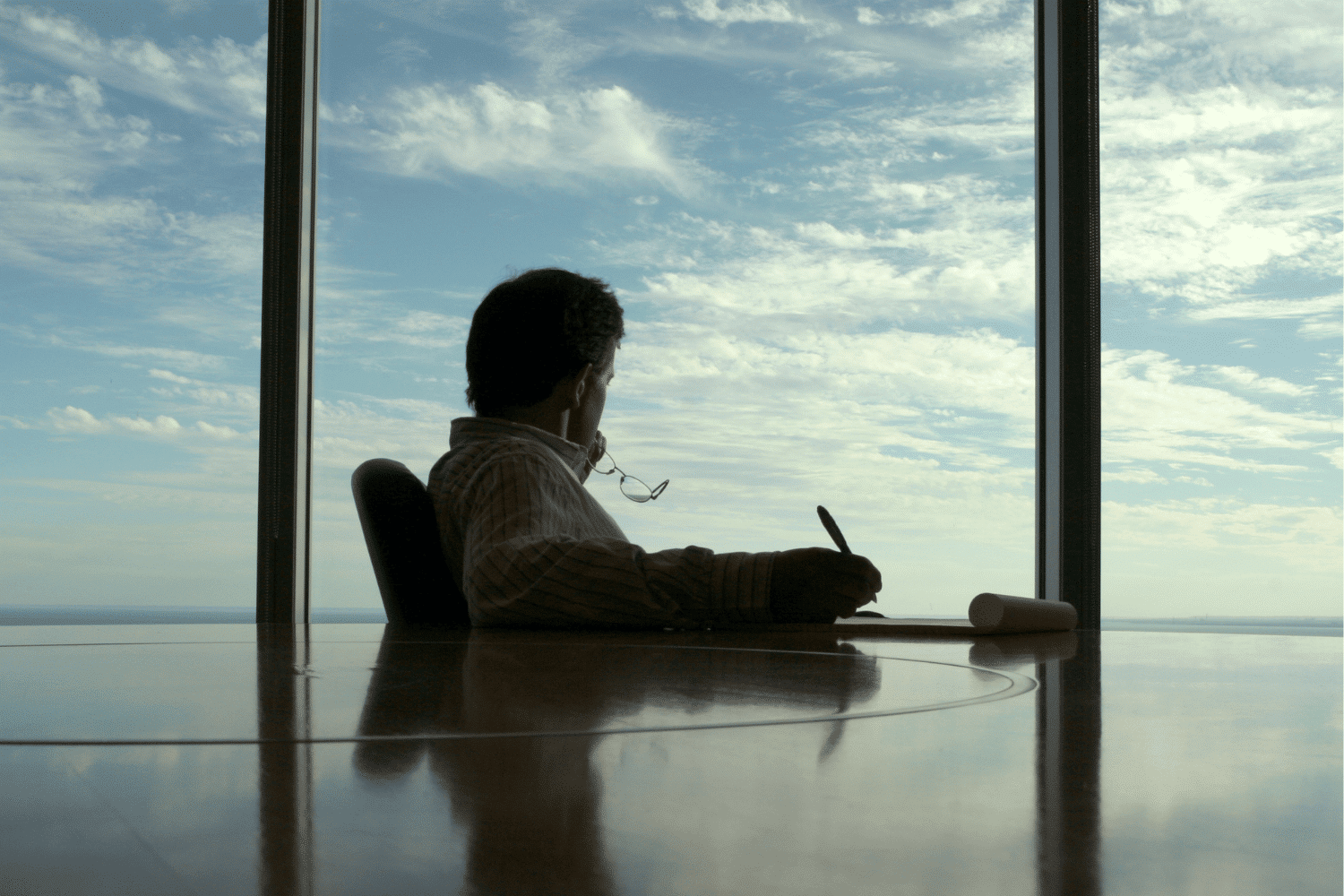 Man sitting at a glass conference room table looking out window