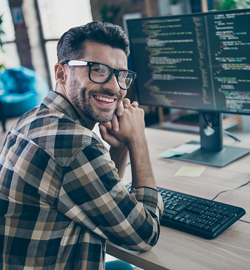 computer programmer in glasses in front of computer screens