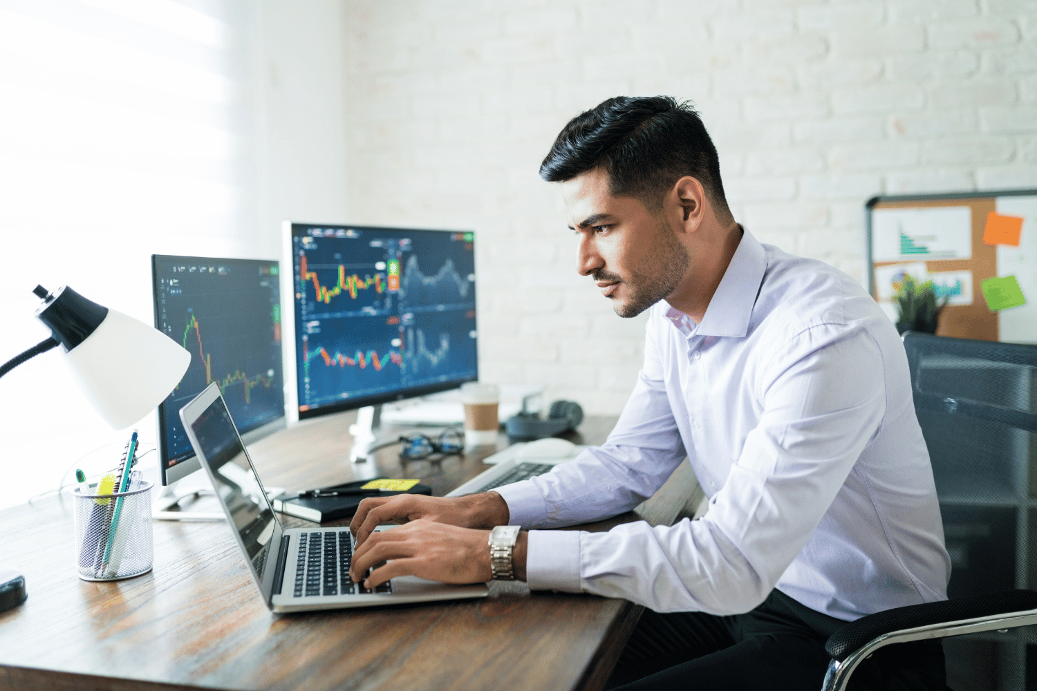 Young businessman working on financials on multiple computer screens