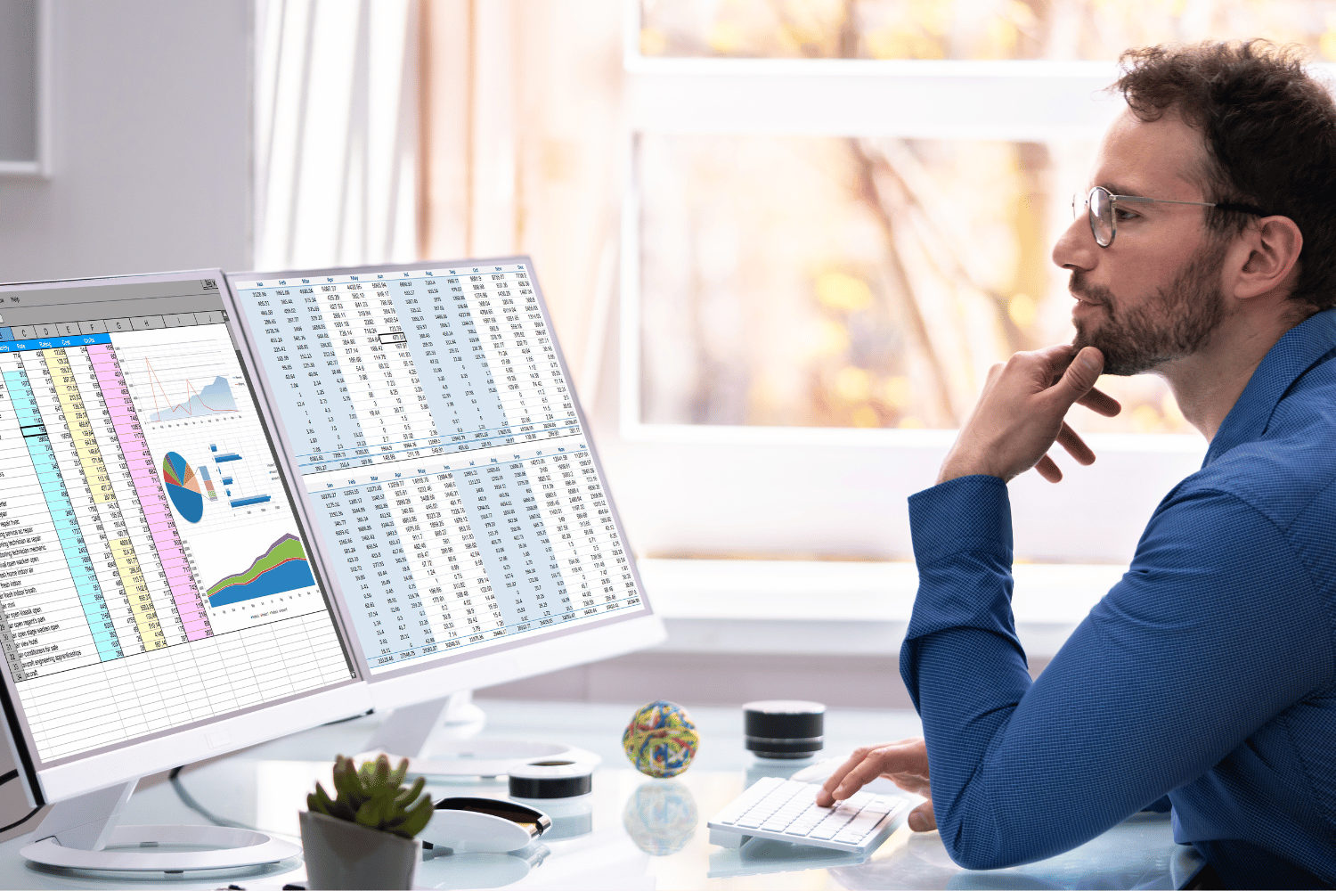 bearded young professional analyzing financial data on dual computer screens