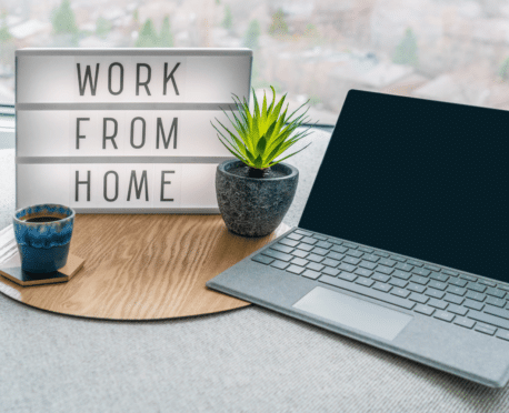 home desk with laptop computer, coffee cup, plants, and sign that says "work from home"