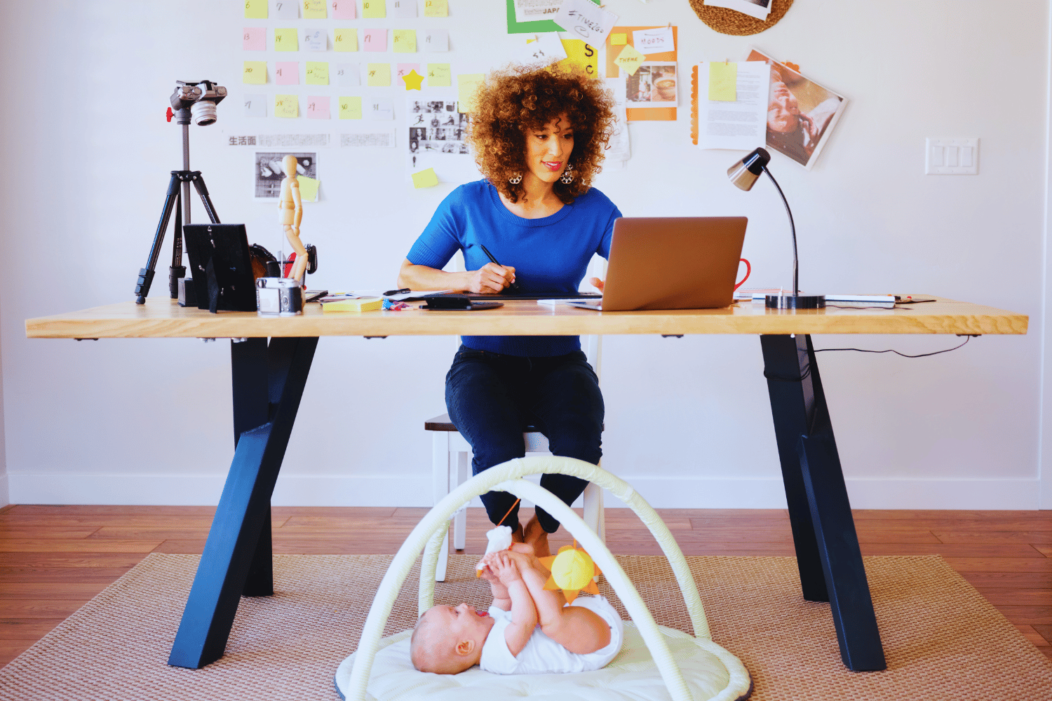 Woman working at home on computer with baby playing on the floor buy her feet