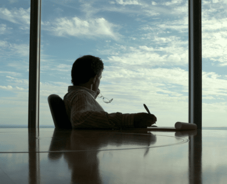 Man sitting at a glass conference room table looking out window