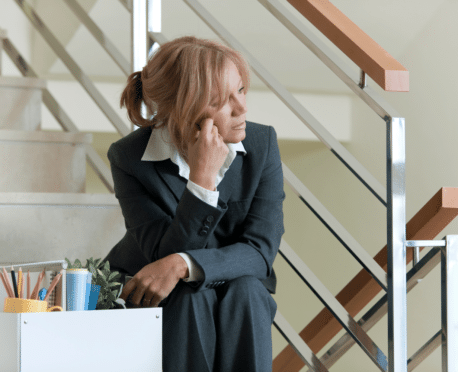 discouraged woman sitting on office stairs with box of belongings after being fired