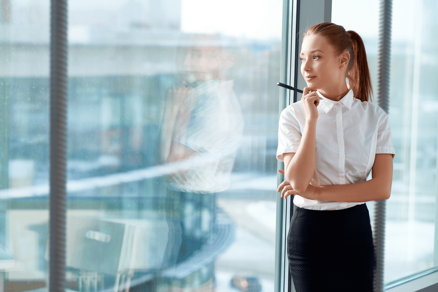 Young professional woman looking out office window, thinking about her dream job