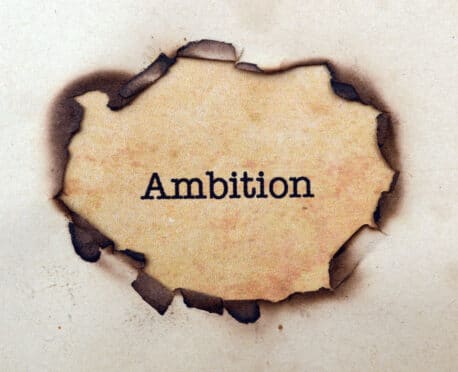 paper with hole burned in it revealing the word Ambition
