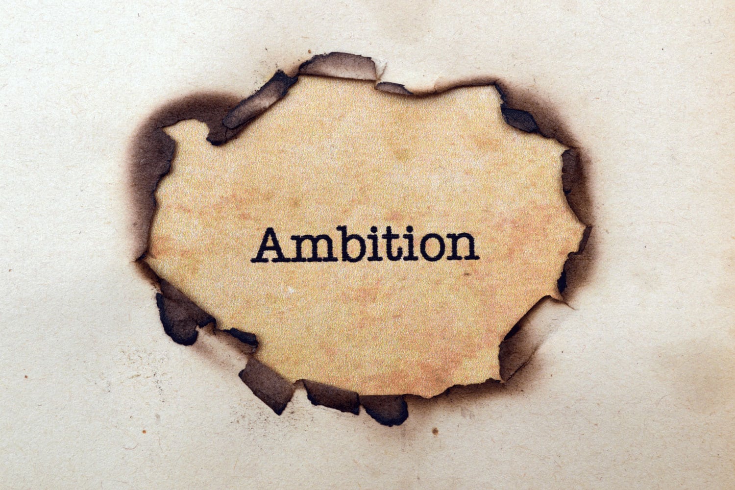 paper with hole burned in it revealing the word Ambition