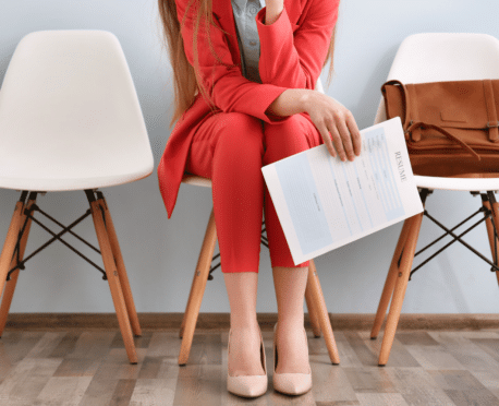 woman from the neck down in red suit sitting in a chair holding a resume