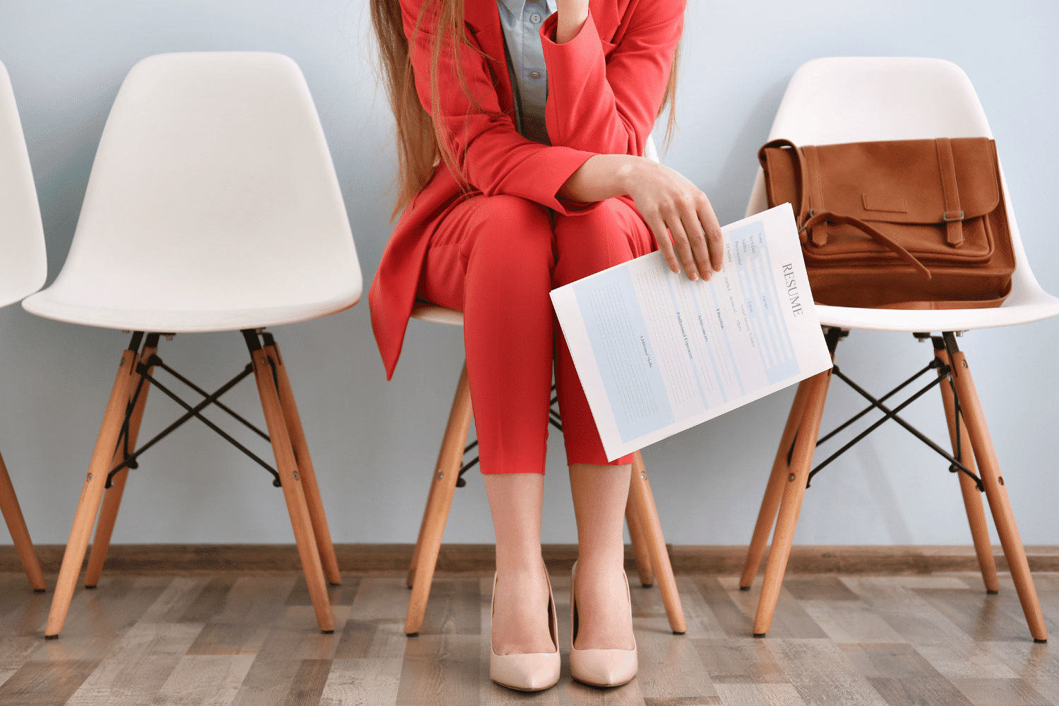 woman from the neck down in red suit sitting in a chair holding a resume