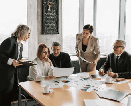 Business meeting with three women and two men discussing financial charts and documents on a conference table, symbolizing high-level executive decision-making and collaboration.