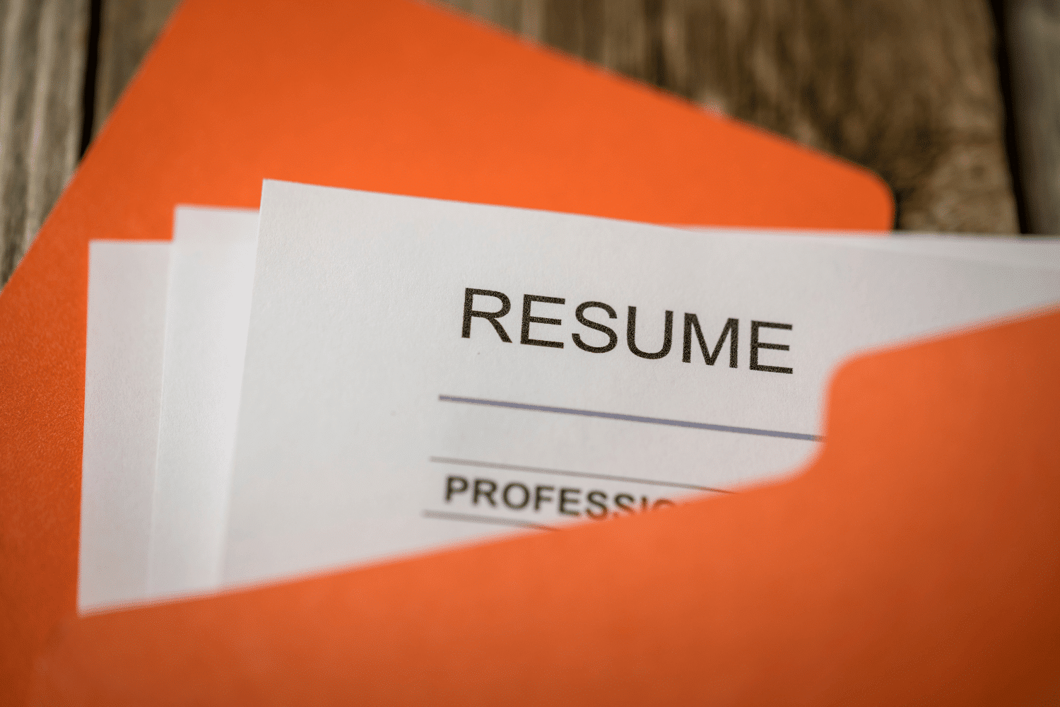An executive resume paper visible inside an orange folder on a wooden desk, representing the process of preparing and submitting professional application documents.