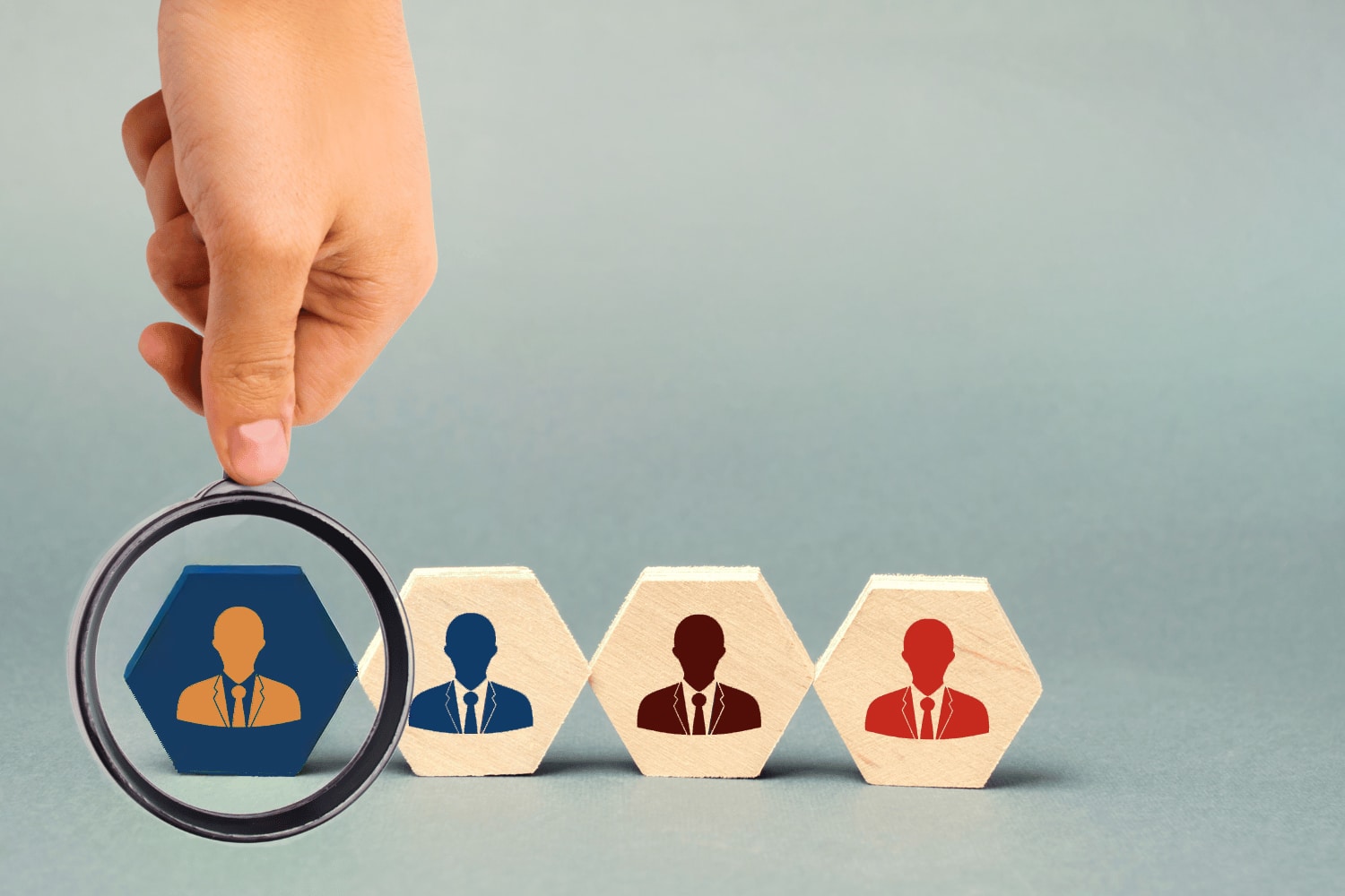 Graphic representation of the executive selection process, showing a magnifying glass examining a highlighted candidate silhouette on a wooden block.