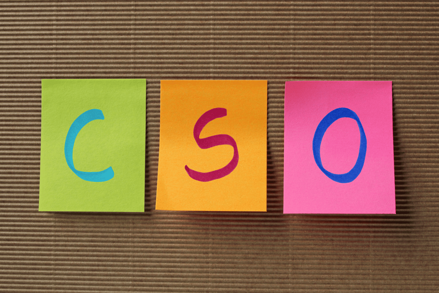 Three colorful sticky notes arranged side by side displaying the letters C, S, and O, representing the acronym CSO (Chief Sustainability Officer)on a textured brown background.