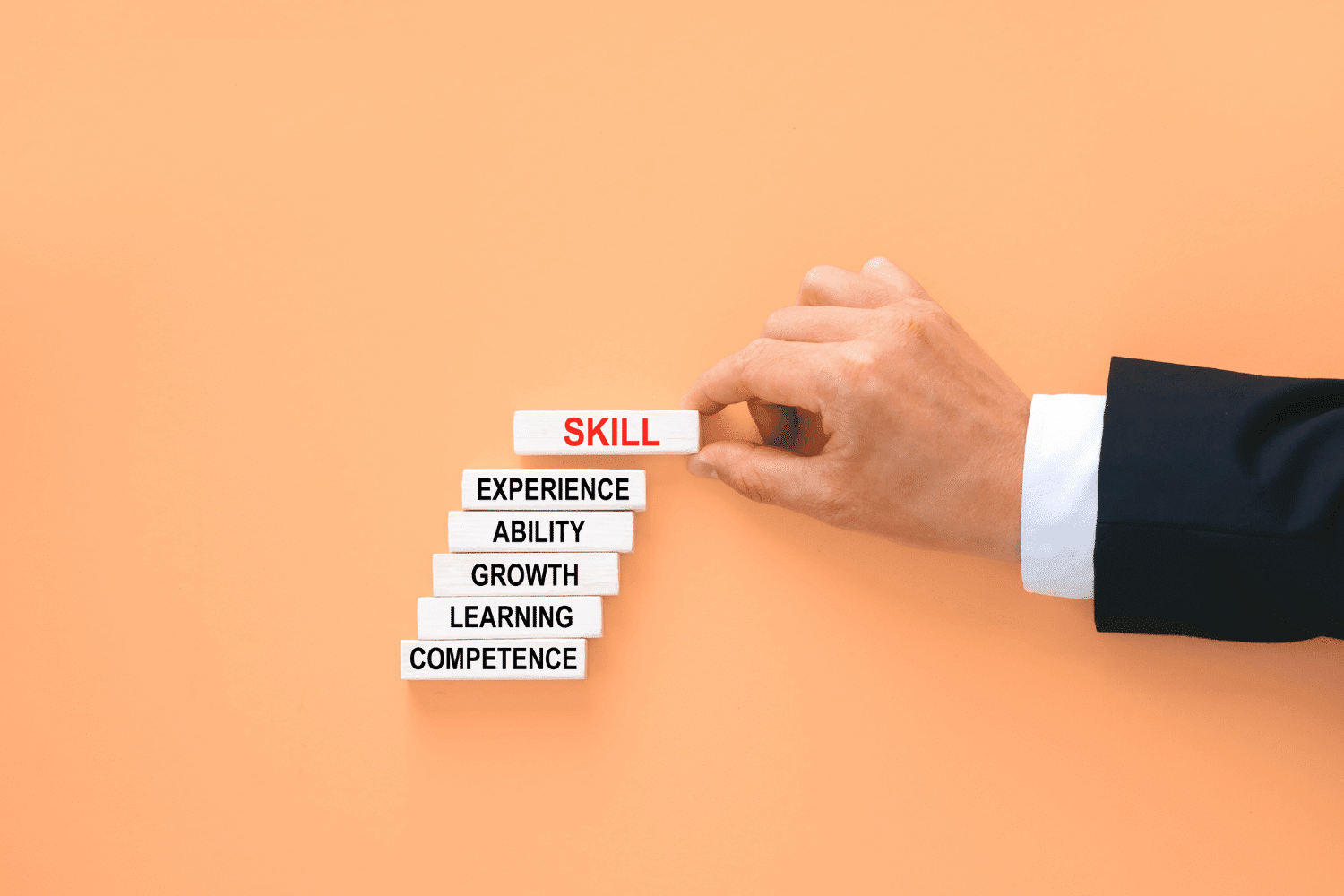 Business leader hand arranging wooden blocks labeled competence, learning, growth, ability, experience, and skill, symbolizing skills-first executive search and outcome-based leadership hiring for Oggi Talent’s blog.