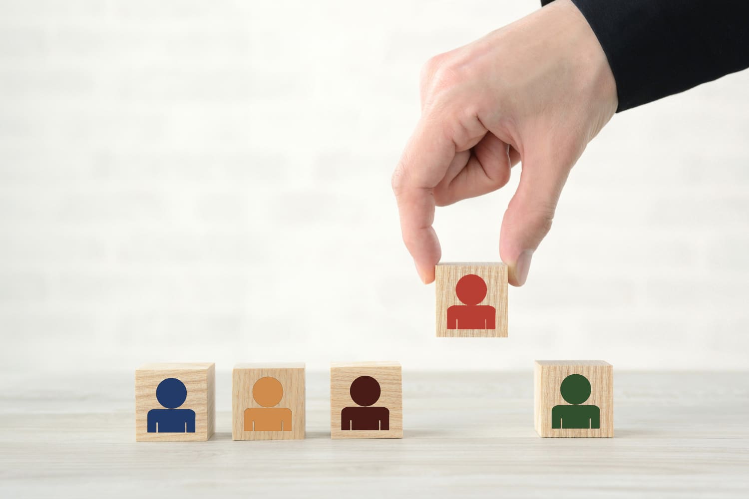 Selective executive hiring concept with hand choosing standout candidate block from diverse row of wooden people icons, symbolizing strategic leadership selection