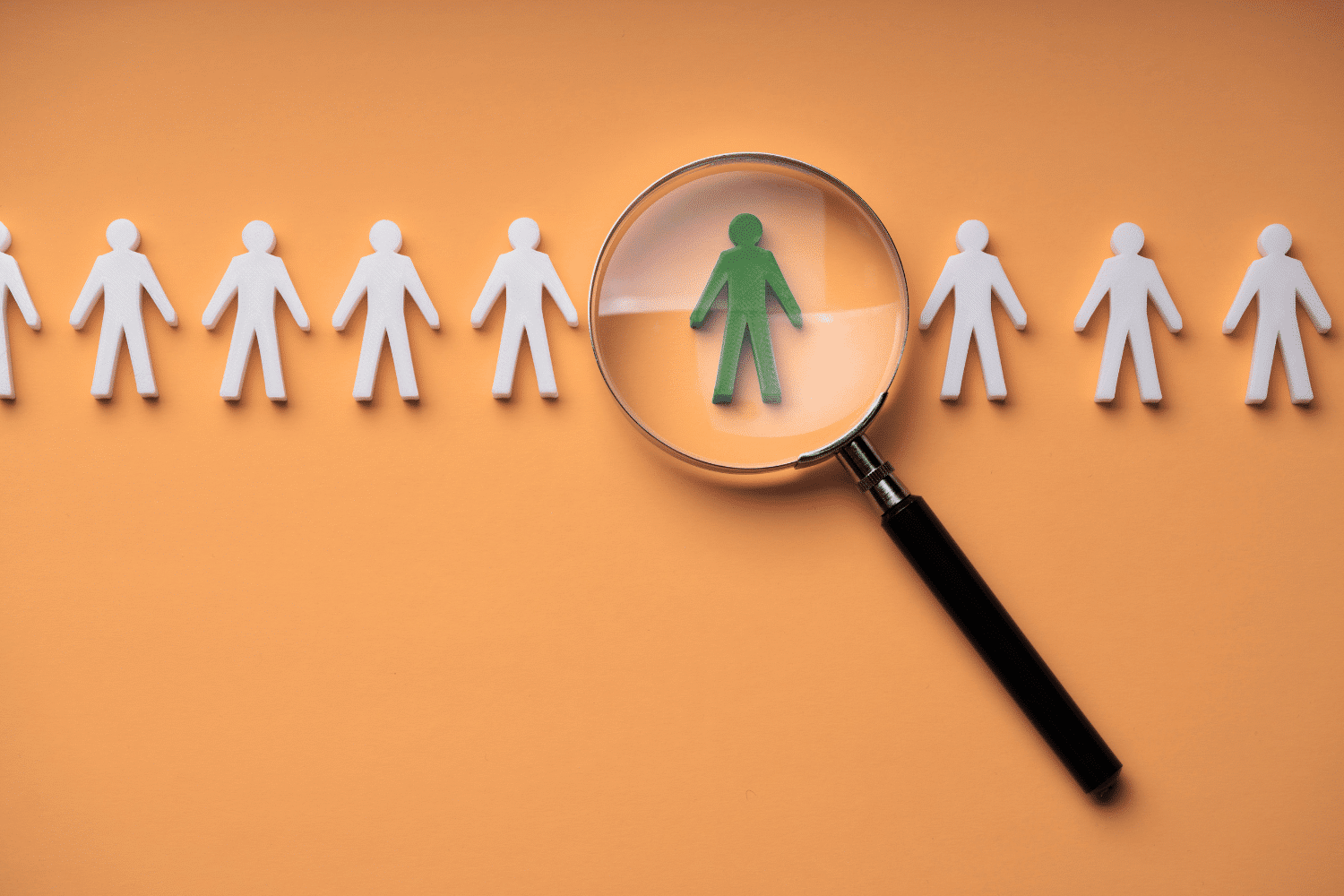 A magnifying glass identifies a distinct green candidate from a general row of white figures, symbolizing the challenges and solutions of CFO succession planning in 2026, and why specialized recruiters are key for Oggi Talent’s hiring strategy.