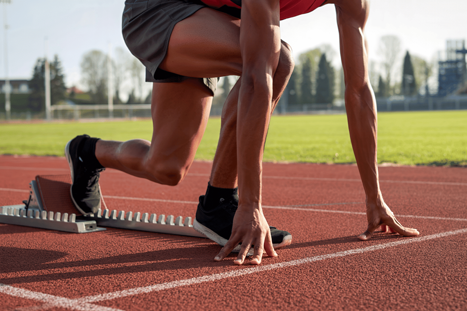 A track athlete in a focused, crouched starting position on a red running track, serving as a powerful visual metaphor for ready on day one executive hiring. This image represents the agility, preparedness, and immediate impact required of modern leaders who are searched and selected to drive organizational success from their first day in a new role.