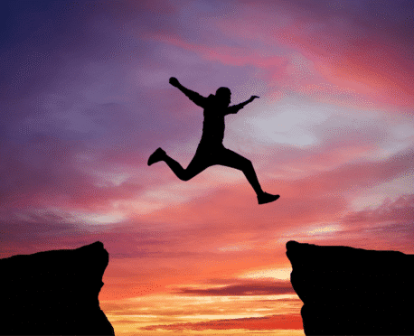 Silhouette of a person jumping between cliffs at sunset, symbolizing a new executive’s transition into leadership
