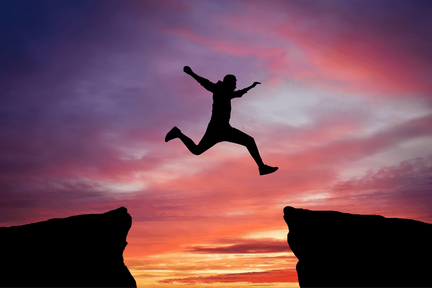 Silhouette of a person jumping between cliffs at sunset, symbolizing a new executive’s transition into leadership